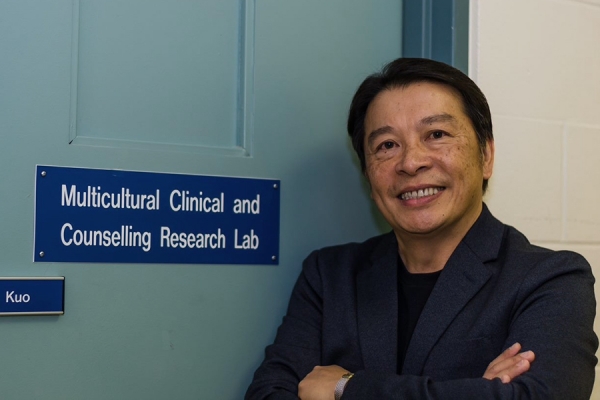 Ben Kuo leaning against door labelled Multicultural Clinical and Counseeling Research Lab