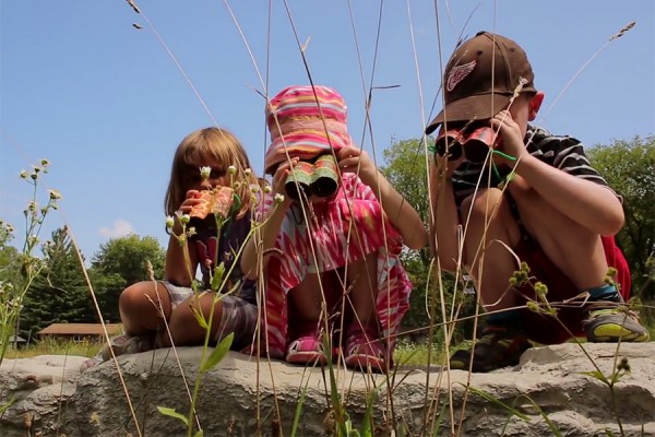 three youngsters looking through binoculars at pond in Ojibway Park