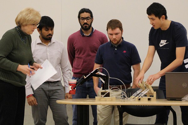 Professor Jill Urbanic looks on as students control a robotic arm to lift a paper cup during final project presentations Thursday in the Centre for Engineering Innovation.