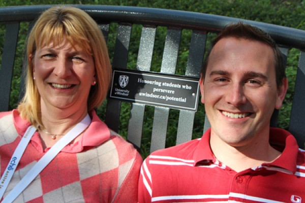 Lorie Stolarchuk and Jonathan Sinasac pose on a bench bearing a plaque promoting a scholarship they set up for students with learning disabilities.