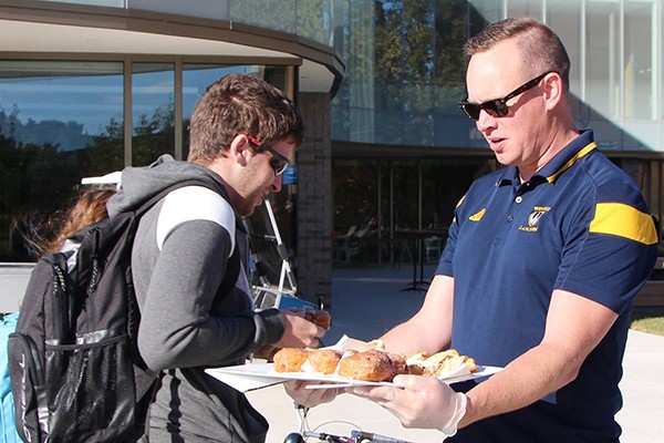 student accepting fritter from Chris Busch