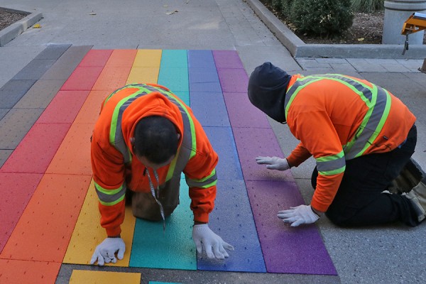 Contractors install Pride colours on the sidewalk outside Dillon Hall.