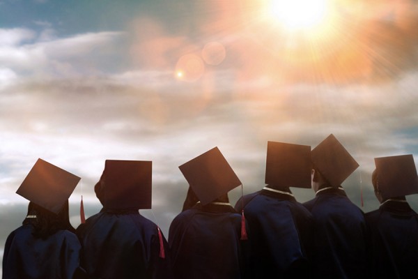 Graduates in mortarboards silhouetted against sunny sky