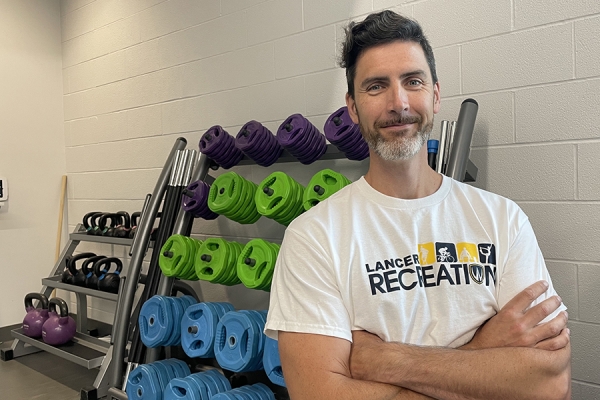 Mike McMahon stands with arms crossed in front of free weights.