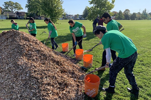 Students shovel mulch to place around newly-planted trees in Gignac Park.