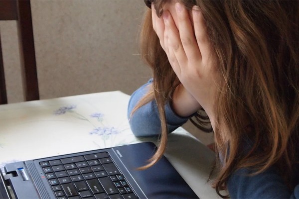 person looking at computer screen with head in hands