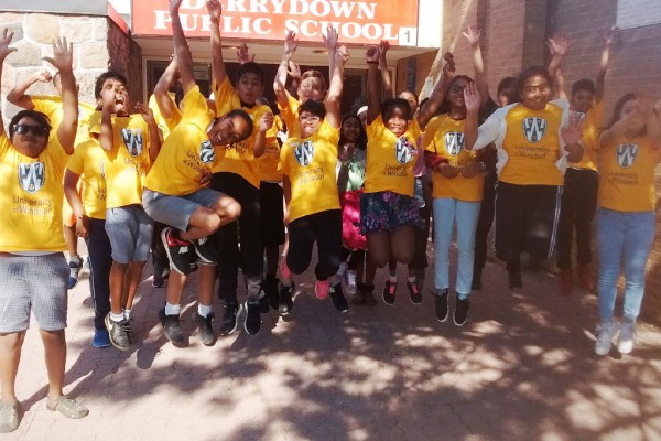 Students at Derrydown Public School inToronto jump in the air while wearing yellow University of Windsor t-shirts.