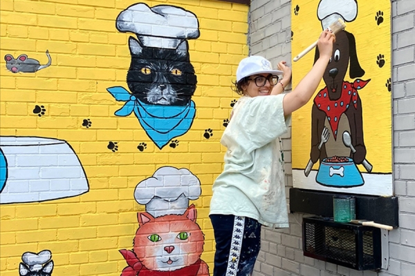 Batool Yahya paints a mural of a dog in a chef hat