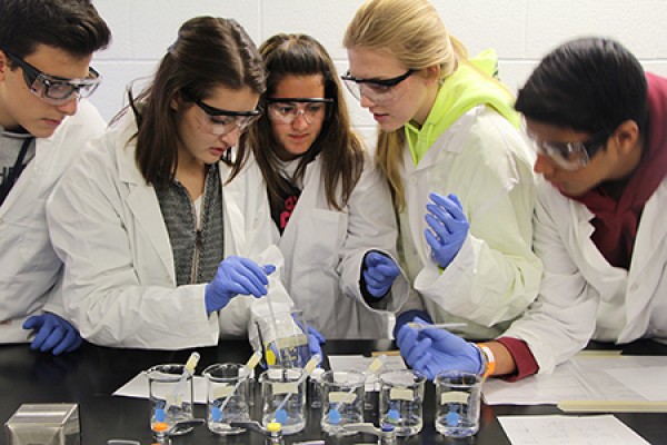 students in lab coats looking over beakers