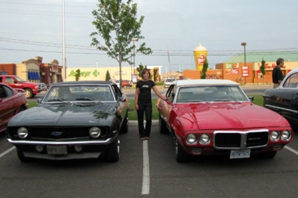 Woman poses between two 1969 muscle cars.