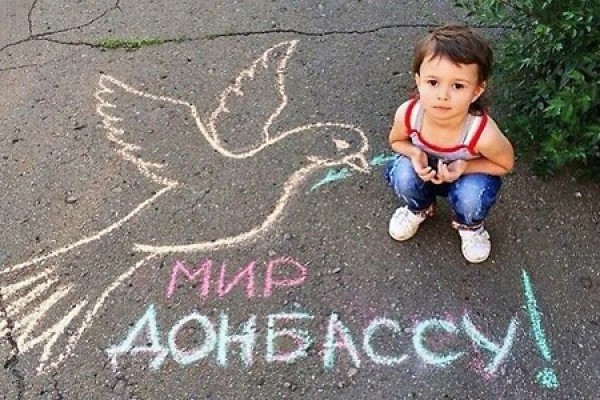 A boy poses next to a chalk drawing expressing the wish for peace for Donbass.