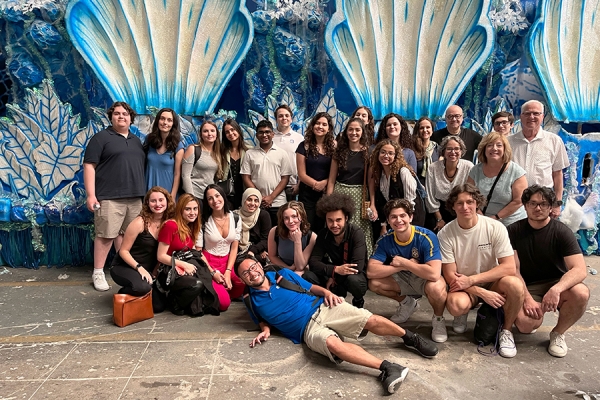 group of students and professors posing in front of wall sculpture of shells