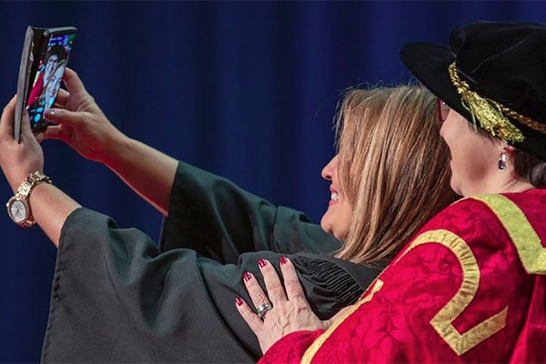 A happy grad poses for a selfie with chancellor Mary Jo Haddad.