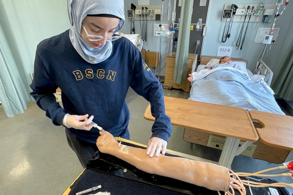 Nursing student Reem Boudali inserts needle into rubber dummy arm.