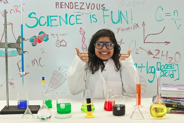 girl in lab coat behind tabel filled with scientific paraphenalia