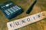 Scrabble tiles spell funding next to calculator