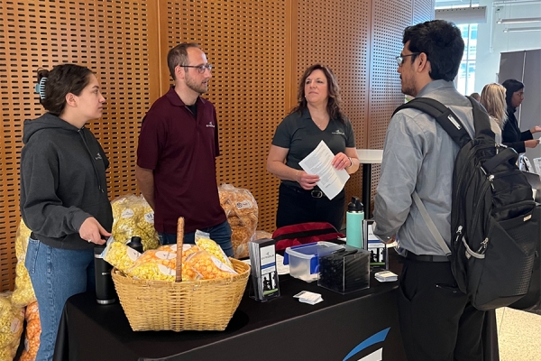 student speaks with three professionals standing behind a display table