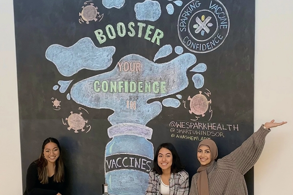 Artists Elyssa Biscocho, Paola Noriega Flores, and Aya El-Hashemi pose with their chalk mural