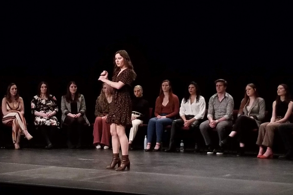 Olivia Ridpath on stage with classmates seated behind