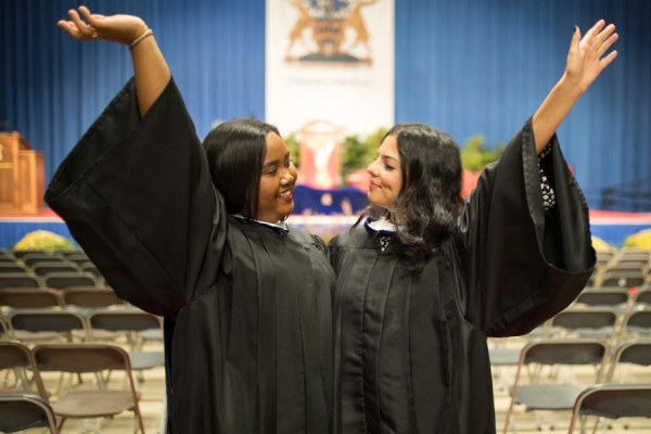 two young women in convocation robes raising hands in celebration