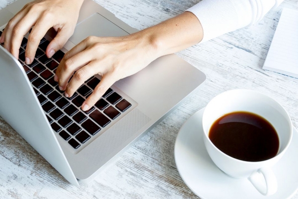 hands on computer keyboard, cup of coffee nearby