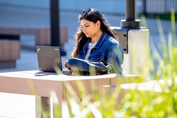 student working on laptop outside campus building