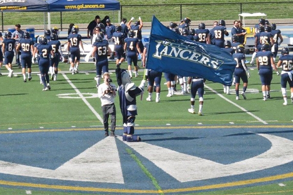 Windsor Lancers mascot Winston holds Lancer flag at football game.
