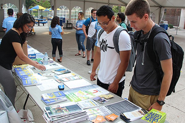 Event coordinator Amber Shaheen gathers some UWindsor Welcome Week material for Luc Nguyen and Derek McCaffrey at the info station, set up in the tent between Memorial and Dillon halls.