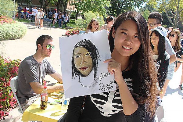 Business major Melissa Li receives a free portrait by artist James Masse during 2015 welcome week activities.