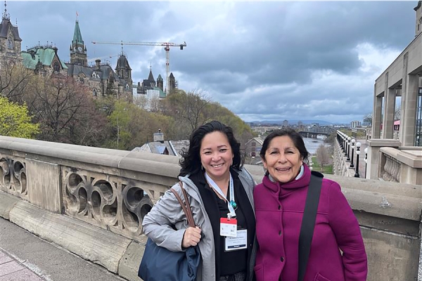 Catherine Febria and Rosa Galvez standing over Rideau Canal, with Parliament buildings in distance