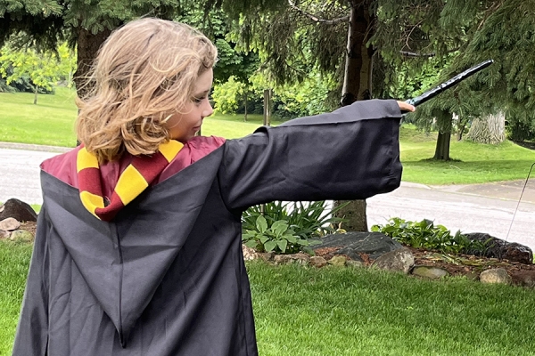 child in Hogwarts robe costume wielding wand