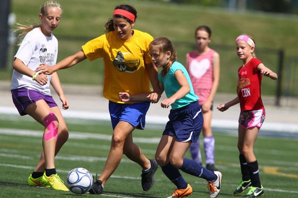 counsellors and kids kick soccer ball at camp