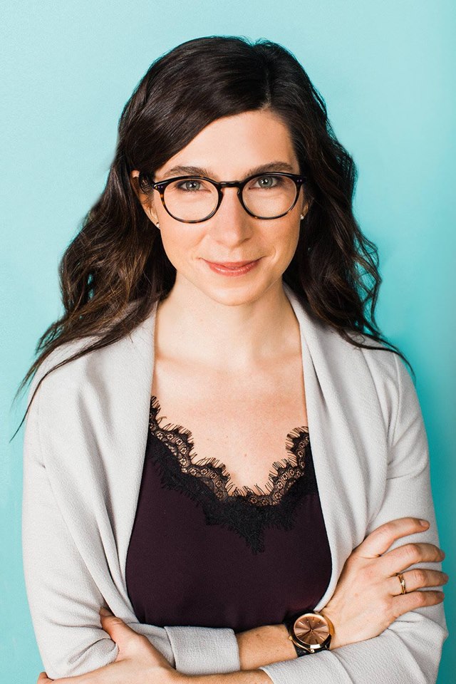 Michelle Macarthur, Assistant Professor. A woman wearing glasses looks into the camera with a smile and folded arms.