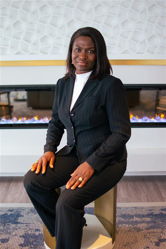 Front/side profile of Dr. Atinuke Adeyemi in business casual attire sitting and smiling at camera