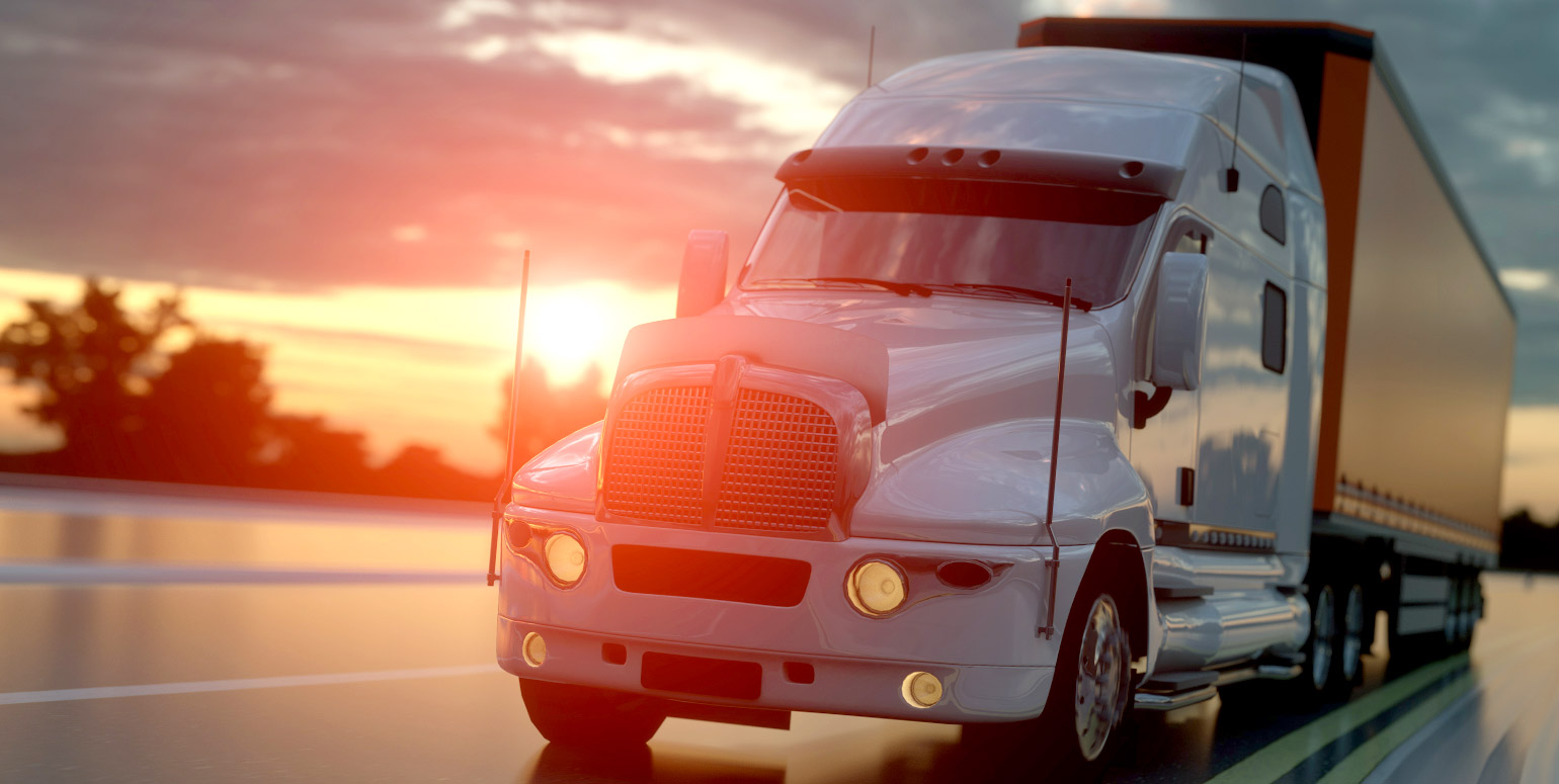 Front view of semi-tractor trailer with sun setting in background