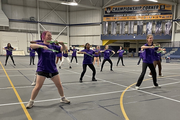 Girls in purple T-shirts hold drum sticks during a pound fit exercise class.