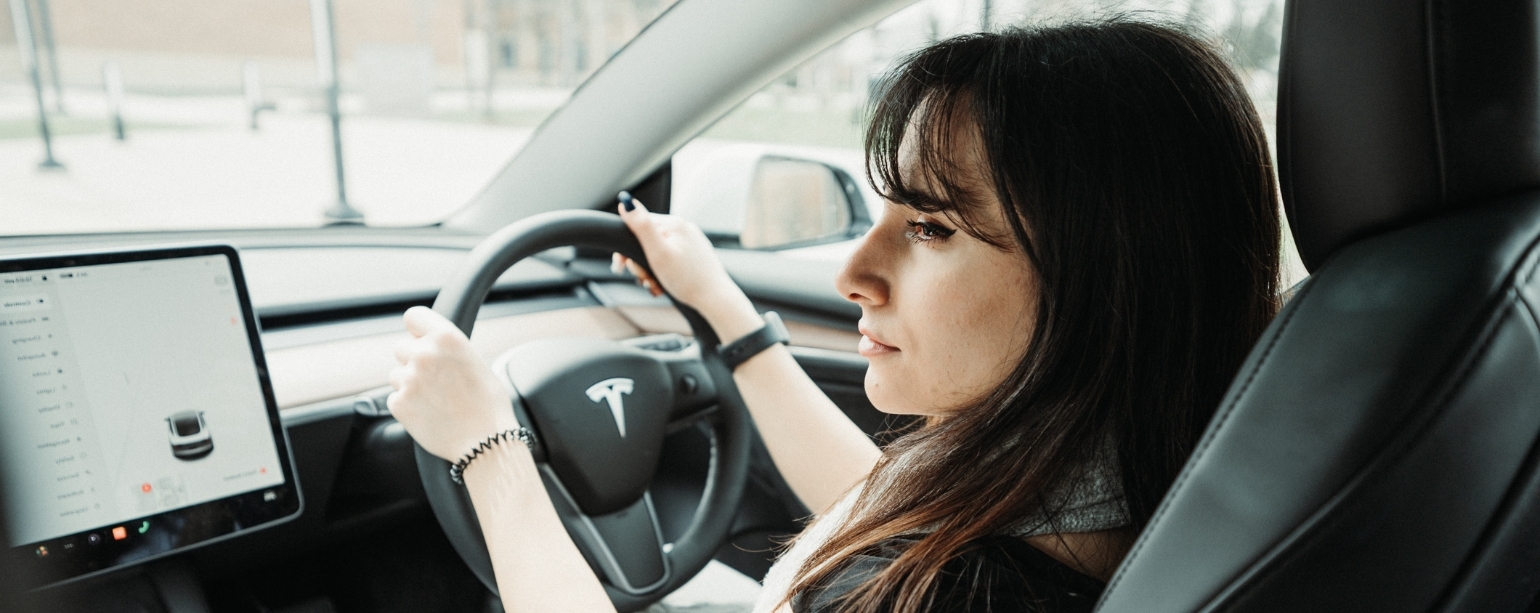A dark-haired woman behind the wheel of a Tesla