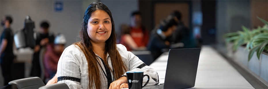 Smiling student with a mug and laptop inside a conference room