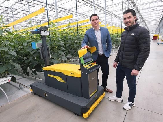 Two people standing in front of a machine in a greenhouse
