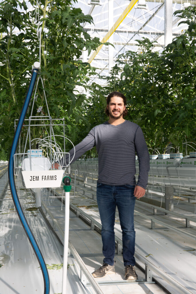 Person standing beside a JEM Farms sign in a greenhouse