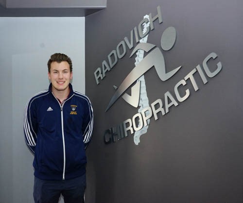 A man standing by a sign, smiling at the camera