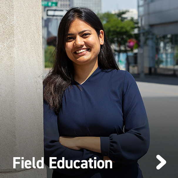 Student leaning up against a concrete pole outside a downtown building in business district