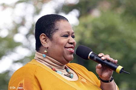 Image of Shahida Nurullah singing into a microphone in performance