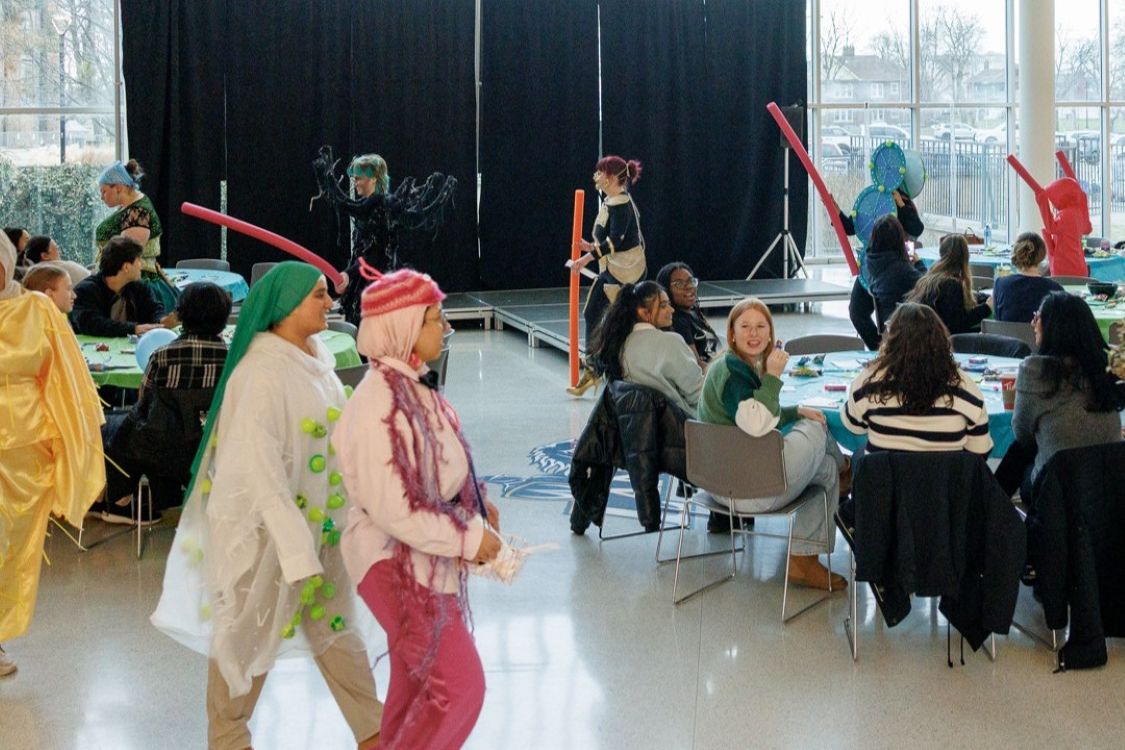 A group of students dressed in various microbe waving pool noodles parade around the CAW student centre