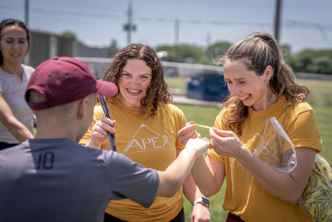 Two young women in yellow t-shirts hand out freezies and bracelets to high school students