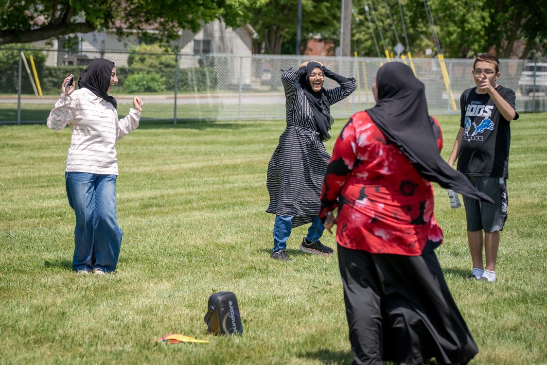 Three teenage girls wearing hijabs smile and laugh with a teenage boy wearing a Detroit Lions shirt