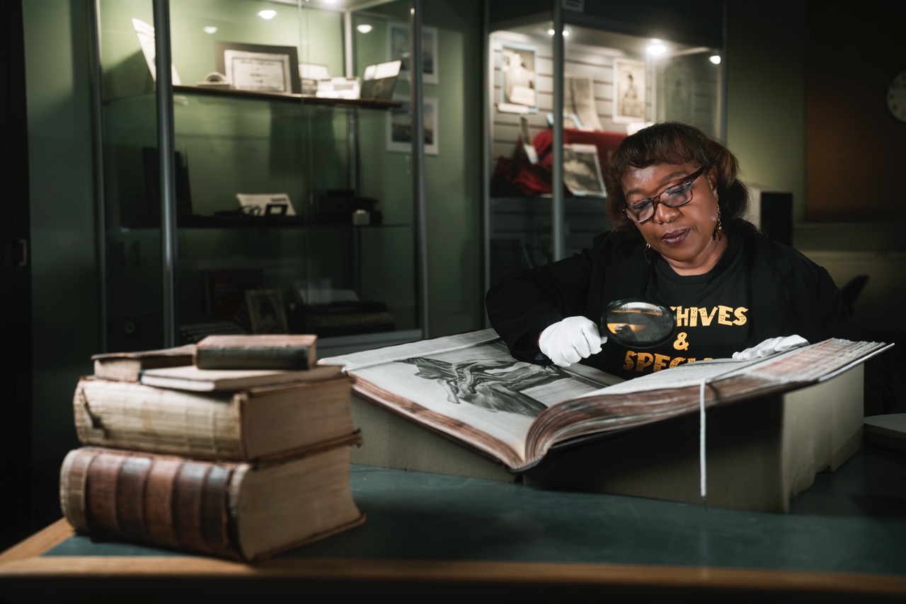 Librarian and archivist Antoinnette Seymour holding a book on a bookshelf UWindsor’s Leddy Library