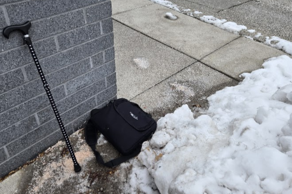 A cane and a bag next to a snow covered sidewalk