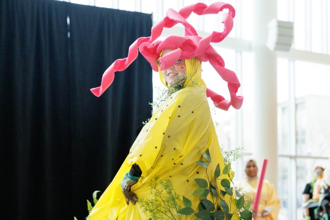 Student dressed in a yellow raincoat covered in fake leaves with spiralled pink pool noodles on their head