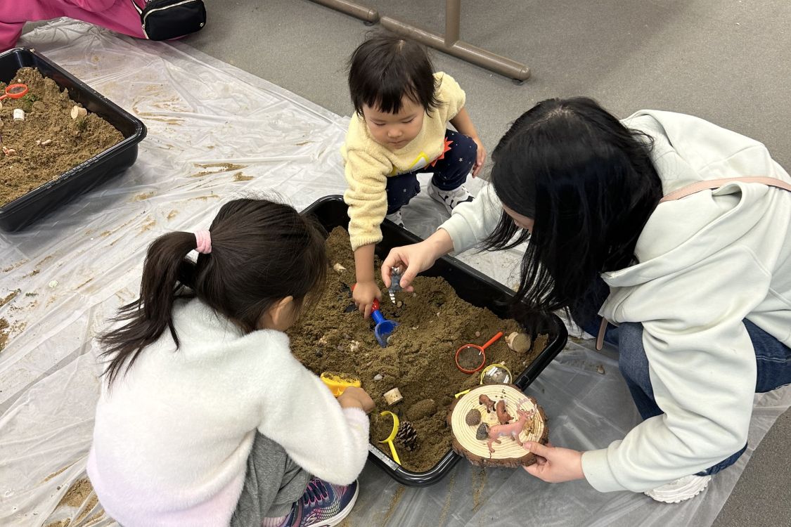 Two small children and an adult dig in a sandbox 
